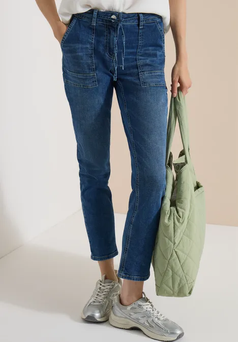 Hüfthohe, dunkelblaue Jeans mit Bündchen, grauen Sneakern und einer hellgrünen, gesteppte Tasche.