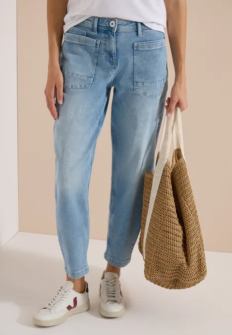 Person trägt helle Jeans, weiße Sneaker und hält eine geflochtene Strohtasche.