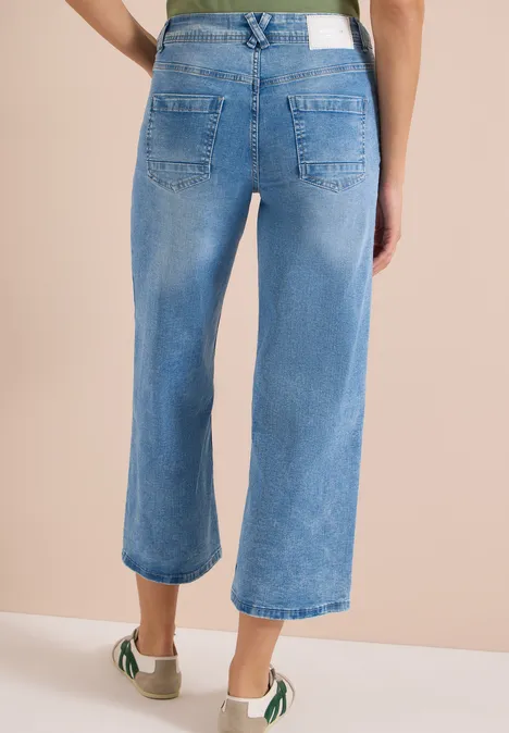 Rückansicht einer Person in hellblauen, weit geschnittenen Jeans und weißen Sneakers