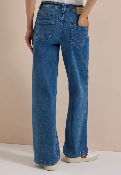 Rückansicht einer Person in weiten, blauen Jeanshosen aus Denim mit aufgesetzten Taschen und geradem Bein.
