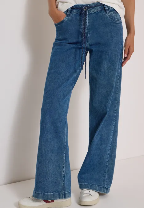 Person trägt blaue, weite Jeans mit hohem Bund und weißen Sneakers.