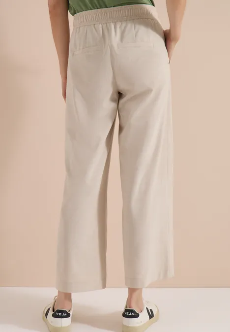 Broek met High Waist en Wide Leg pijpen in een Loose Fit pasvorm cashmere beige melange Achteraanzicht van iemand in beige, wijde broek met elastische taille en zwarte espadrilles.
