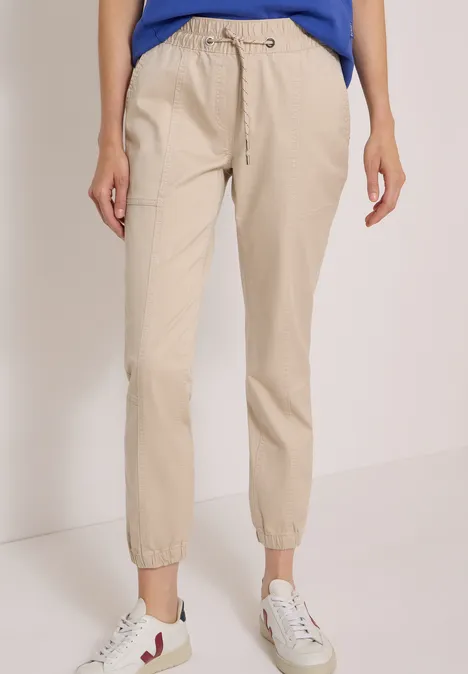 Beige Damen-Jogginghose mit Kordelzug, Gummizugbund und -bündchen, kombiniert mit weißen Sneakern.