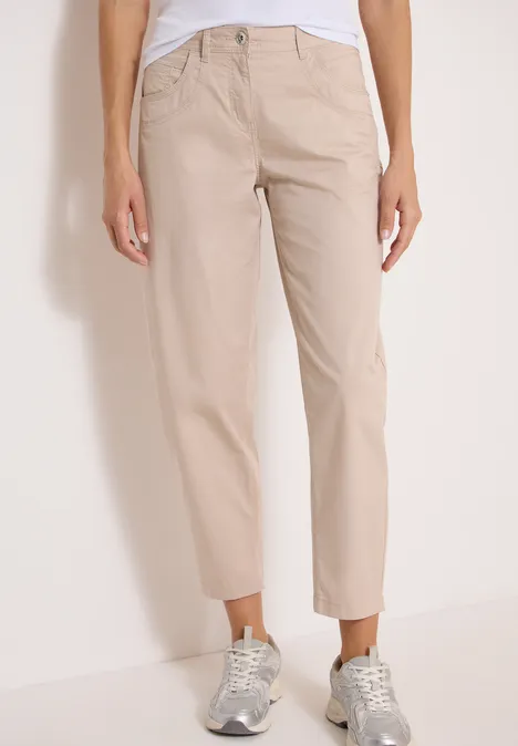 Spodnie z szerokimi nogawkami z tkaniny o fakturze papieru cashmere beige Ujęcie nóg w beżowych, prostych, casualowych spodniach i srebrnych tenisówkach.