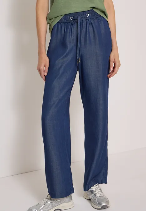 Weit geschnittene, hoch taillierte, dunkelblaue Hose mit Tunnelzug und silbernen Sneakern.
