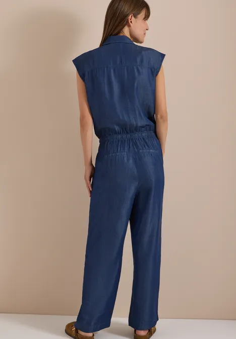 Rückansicht einer Frau in einem ärmellosen, dunkelblauen Jeans-Jumpsuit.