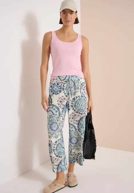 High Waist Wide Leg Hose w kroju Loose Fit vanilla white Kobieta w różowym topie, wzorzystych niebieskich spodniach, beżowych butach i czarnej torbie.