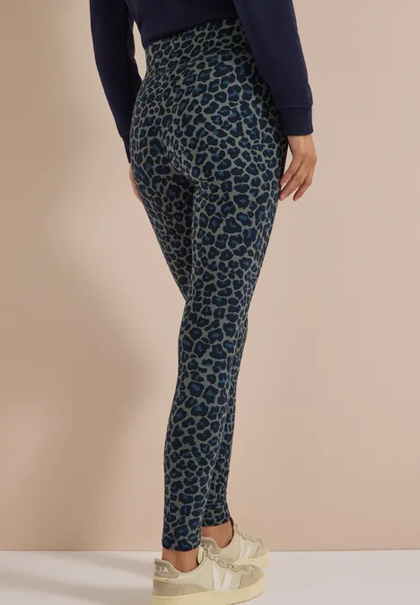 Legging met luipaardprint dried olive green Een persoon draagt blauwe legging met donkerblauw luipaardpatroon en lichte sneakers voor een beige achtergrond.
