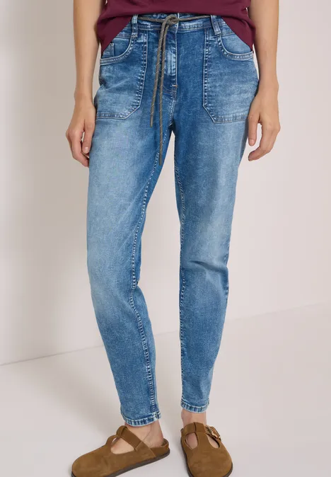 Eine Person trägt lässige blaue Jeans mit Tunnelzugtaillenband und Taschen, kombiniert mit Sandaletten.
