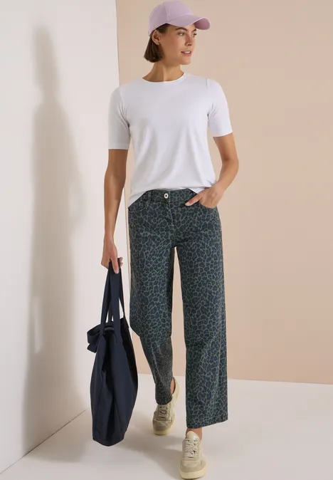 Kobieta w białym t-shircie, luźnych wzorzystych spodniach, czapce, trzyma dużą torbę materiałową.