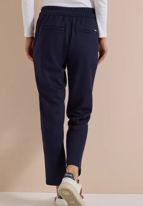 Pantalon taille mi-haute, coupe Slim Leg et style décontracté urban dark blue Rückansicht einer Person in dunkelblauen Jogginghosen und Sneakern vor beigem Hintergrund.