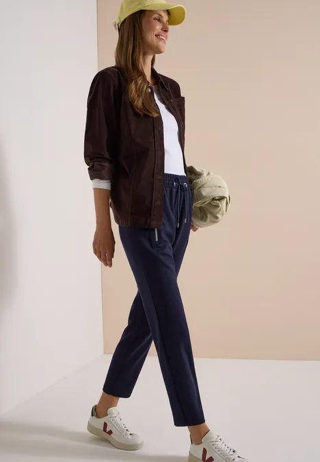 Pantalon taille mi-haute, coupe Slim Leg et style décontracté urban dark blue Eine Frau in grüner Kappe, brauner Jacke, weißem Shirt, blauen Hosen und weißen Sneakers hält eine Tasche.