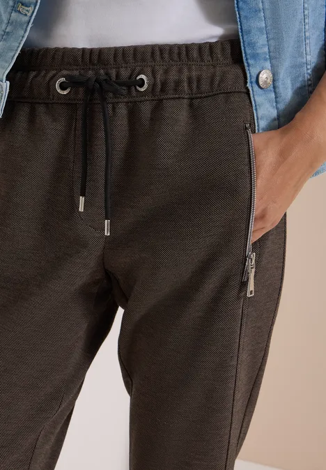 Pantalon taille mi-haute, coupe Slim Leg et style décontracté creamy mocha Dunkle Jogginghose mit Kordelzugbund und seitlichen Reißverschlusstaschen, kombiniert mit Jeanshemd.
