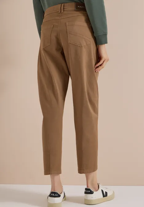 Mid Waist Barrel Leg Hose im Casual Fit creamy mocha Rückansicht einer Person in braunen, knöchellangen Hosen und weißen Slip-on-Sneakern vor beigem Hintergrund