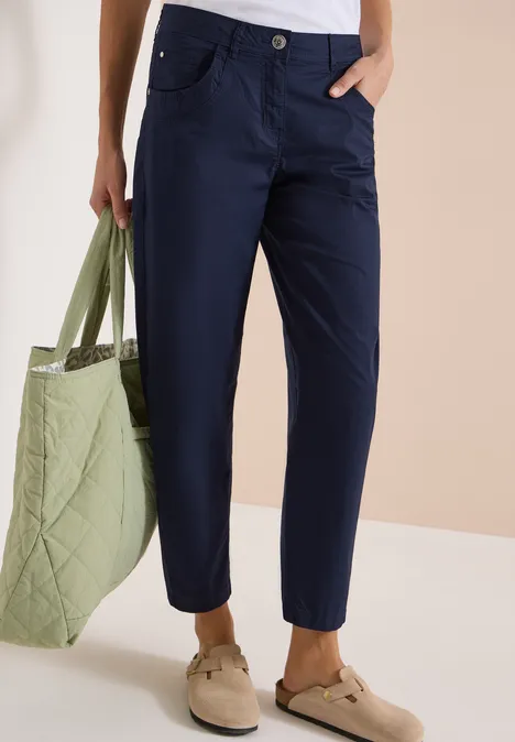 Person trägt dunkelblaue Hose, hält gesteppte grüne Tasche, dazu bequeme beige Schuhe.