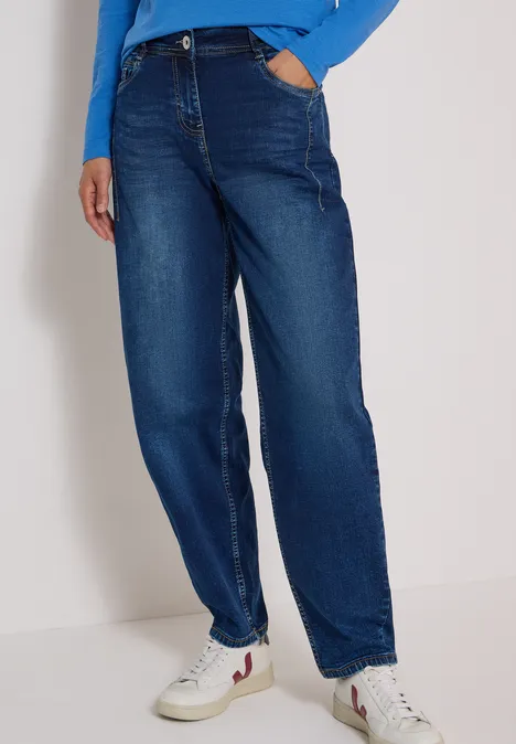 Beine in hoch geschnittener, weiter dunkelblauer Jeans und weißen Sneakern.