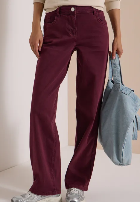 Pantalon ample en velours côtelé bordeaux, haut blanc, baskets argentées et sac en jean bleu clair.
