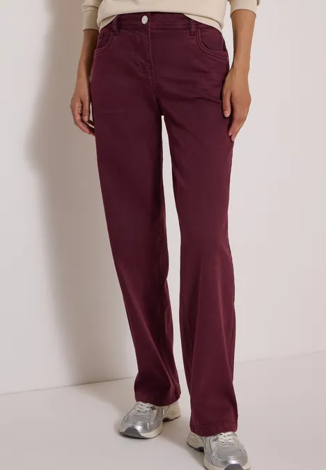 Une personne porte un jean bordeaux taille haute, coupe droite, et des baskets argentées.