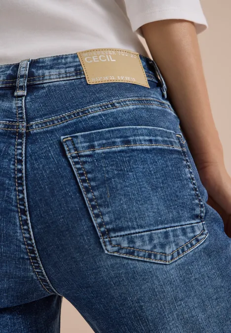 Vue arrière d’une personne portant un jean bleu avec étiquette de marque à la taille.