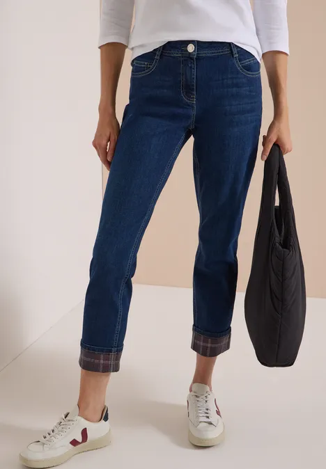 Personne porte un jean bleu foncé retroussé, baskets blanches et un sac noir.