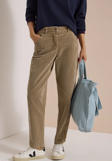 Person trägt hellbraune Cordhose und weiße Sneaker, hält eine blaue Jeansjacke.