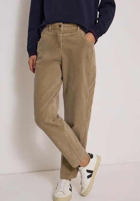 Beige Cordhose mit hohem Bund, Seitentaschen und weißen Sneakern.