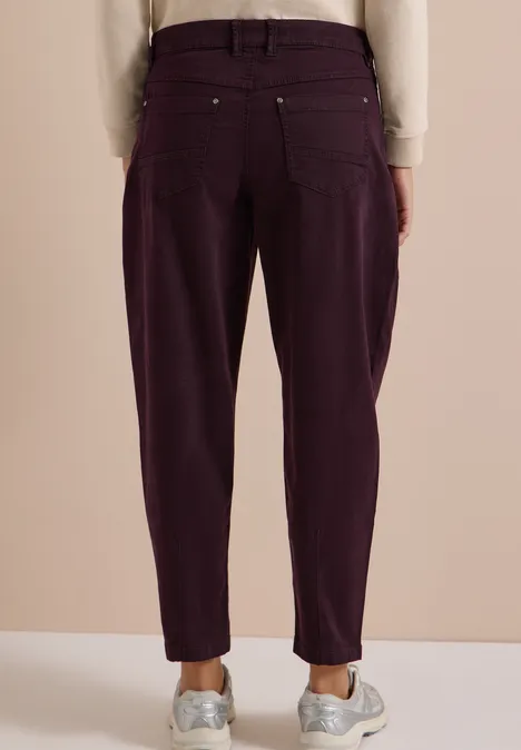 Rückansicht einer Person in lässigen, dunkelvioletten High-Waist-Hosen und weißen Sneakern.