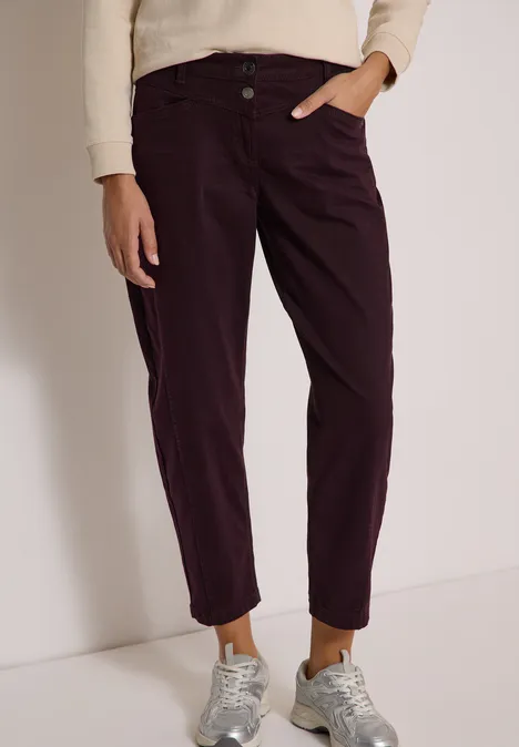 Damenhose in dunklem Aubergine mit umgeschlagenen Säumen, kombiniert mit Sneakern und hellem Pullover.