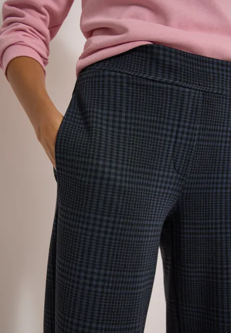 Nahaufnahme einer Person in karierter Hose und rosa Pullover, Hand in Tasche