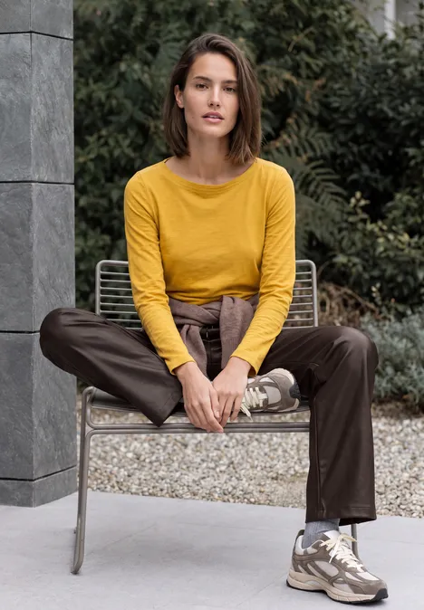 Frau in gelbem Pullover und brauner Hose sitzt entspannt auf einem Outdoor-Stuhl