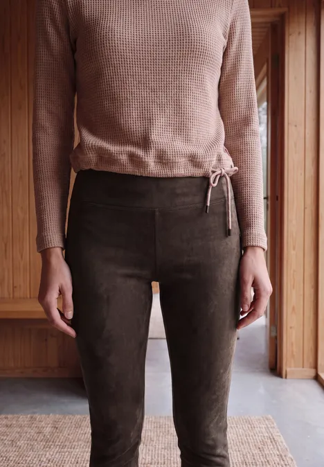 Eine Person trägt ein braunes Langarmshirt und dunkelbraune Hosen in einem Holzinterieur.