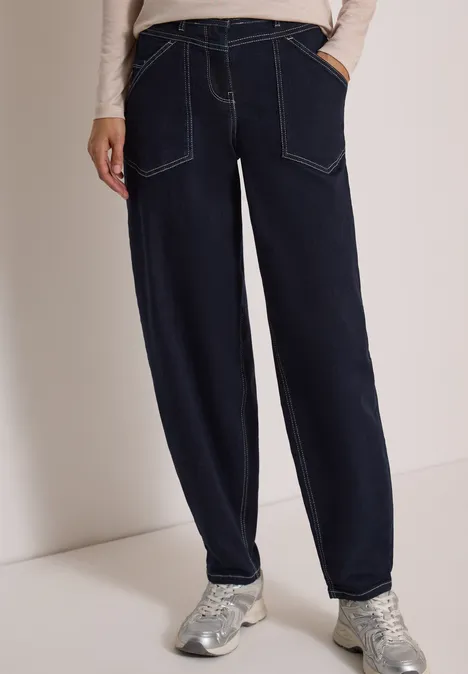 Dunkelblaue, locker sitzende Jeans mit Kontrastnähten und silbernen Sneakern.