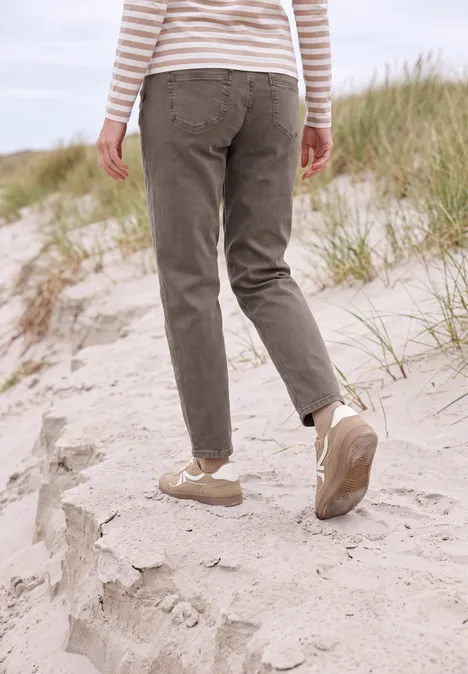 Persoon in gestreept shirt, olijfkleurige broek en beige sneakers loopt over zandduinen