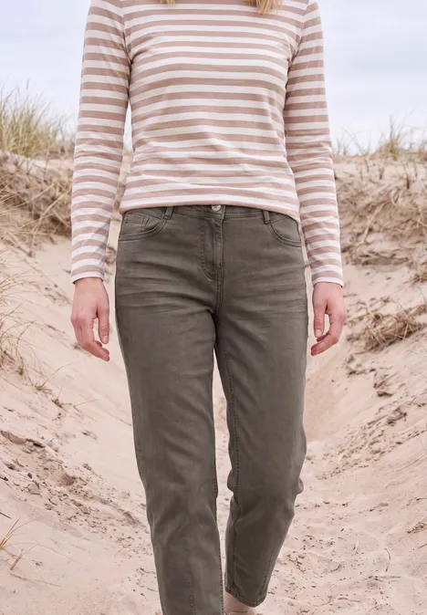 Persoon in beige-wit gestreept shirt en kaki broek loopt over zandduinen, met helmgras op de achtergrond.