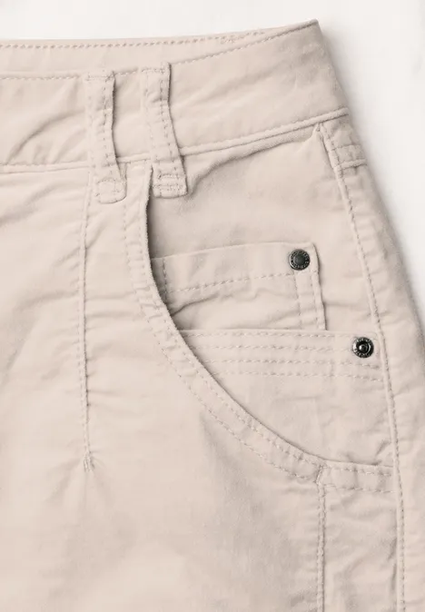 Beige Jeans- oder Stoffhose mit sichtbarer Fronttasche, Gürtelschlaufe und Metallnieten.
