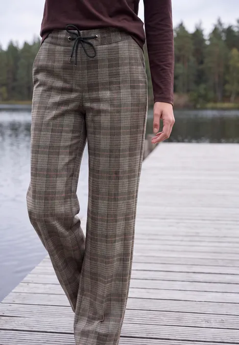 High Waist Wide Leg Hose im Loose Fit truffle brown Eine Person steht auf einem Holzsteg am See und trägt karierte, lockere Stoffhose mit Kordelzug.