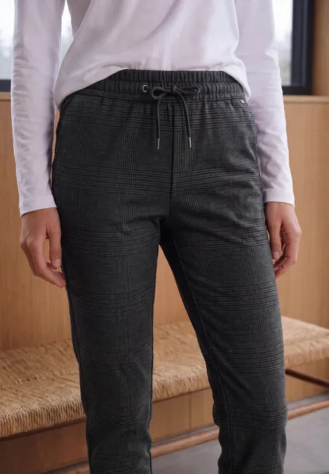 Mid Waist Slim Leg Hose im Casual Fit truffle brown Eine Person trägt eine weiße Langarmbluse und dunkle, gemusterte Jogginghose.