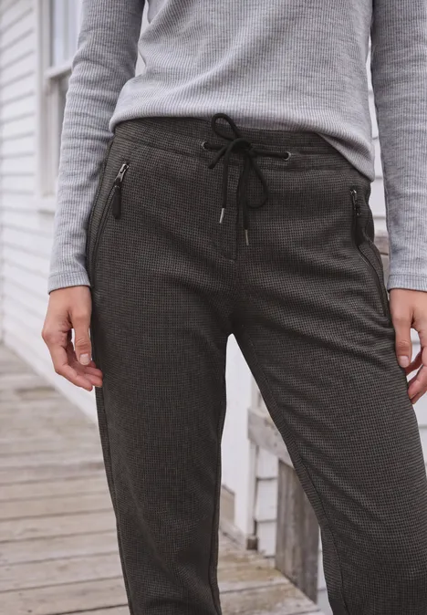 Mid Waist Barrel Leg Hose im Casual Fit creamy mocha Frau trägt grauen Pullover und dunkelgraue Jogginghose mit Reißverschlusstaschen.