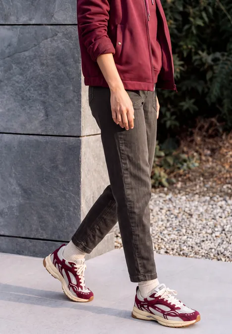 Jeans met wijd uitlopende pijpen in garment-dye-look truffle brown Een persoon staat buiten op steentegels, draagt een zwarte broek en bordeauxrode sneakers met witte sokken.