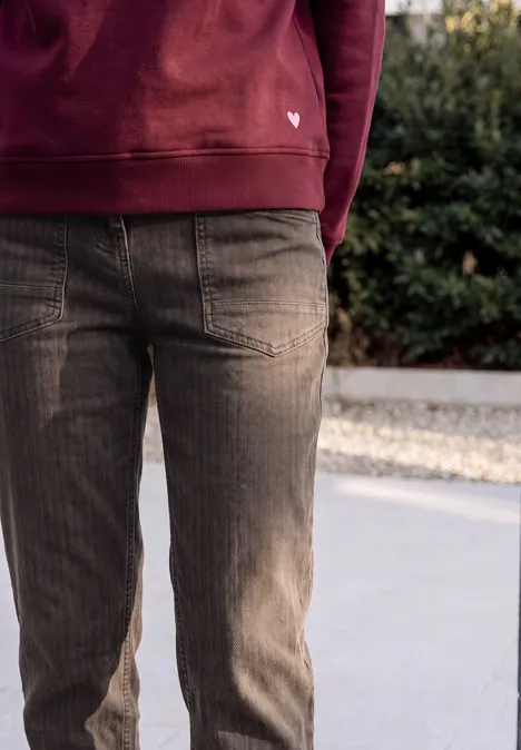Jeans met wijd uitlopende pijpen in garment-dye-look truffle brown Onderlichaam van iemand met rode capuchontrui en bruine corduroy broek op stoep voor struiken.