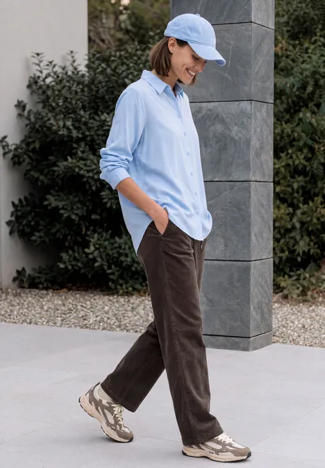 Personne en chemise bleue, pantalon marron et baskets marche en extérieur.