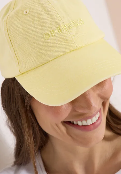 Frau trägt hellgelbe Baseballkappe, Gesicht unscharf