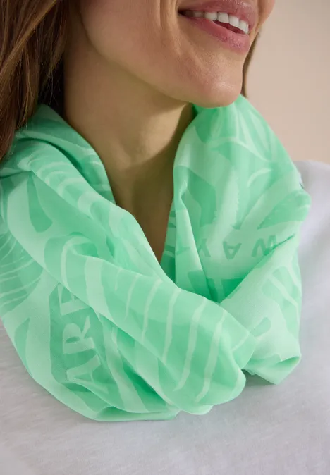 Eine Frau trägt einen neon-grünen Rundschal mit feinem Muster über einem weißen Oberteil.
