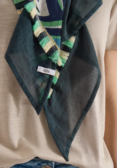 Leichtes, schwarzes Halstuch mit grünen und beigen Fransen, mit “CECIL”-Etikett, getragen über beigem Oberteil.