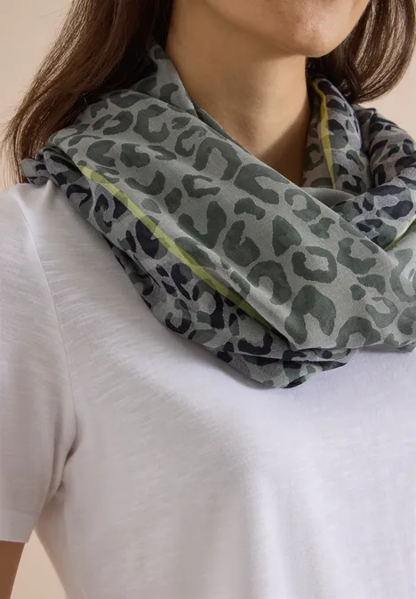 Loop-sjaal in uitgebleekte look met luipaardpatroon dried olive green Graugrüner Loop-Schal mit Leopardenmuster, getragen über einem weißen T-Shirt.