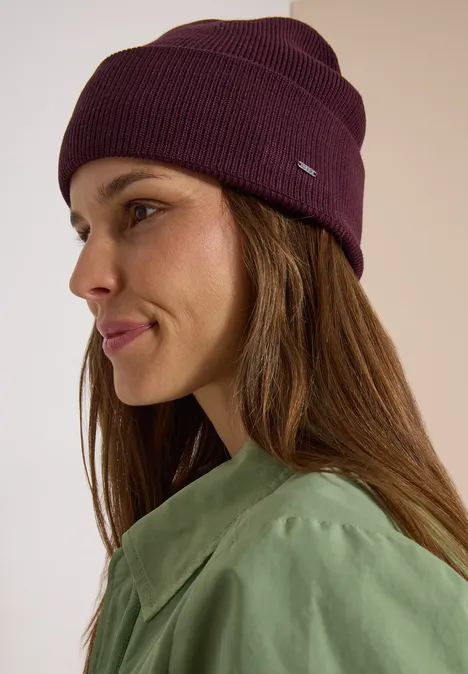 Portrait de profil d'une femme portant un bonnet violet et un haut vert, cheveux bruns longs, léger sourire.