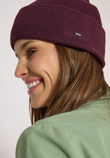 Gros plan d'une femme souriante en veste verte et bonnet violet.