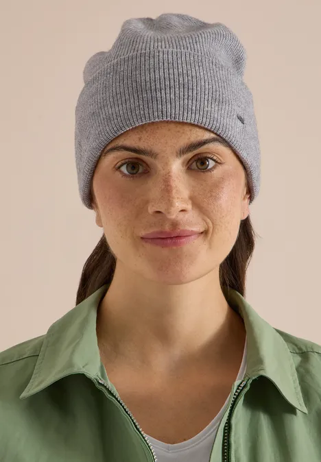 Une femme porte un bonnet gris et une chemise verte, elle sourit légèrement.