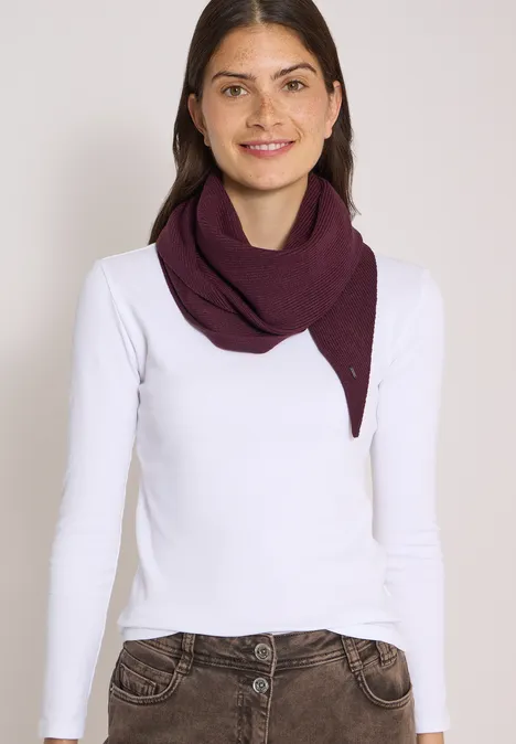 Femme souriante portant un t-shirt à manches longues blanc et une écharpe violette sur fond neutre.