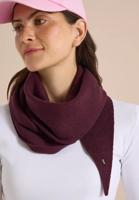 Femme en haut blanc, casquette rose et écharpe tricotée bordeaux, portée en tour de cou décontracté.